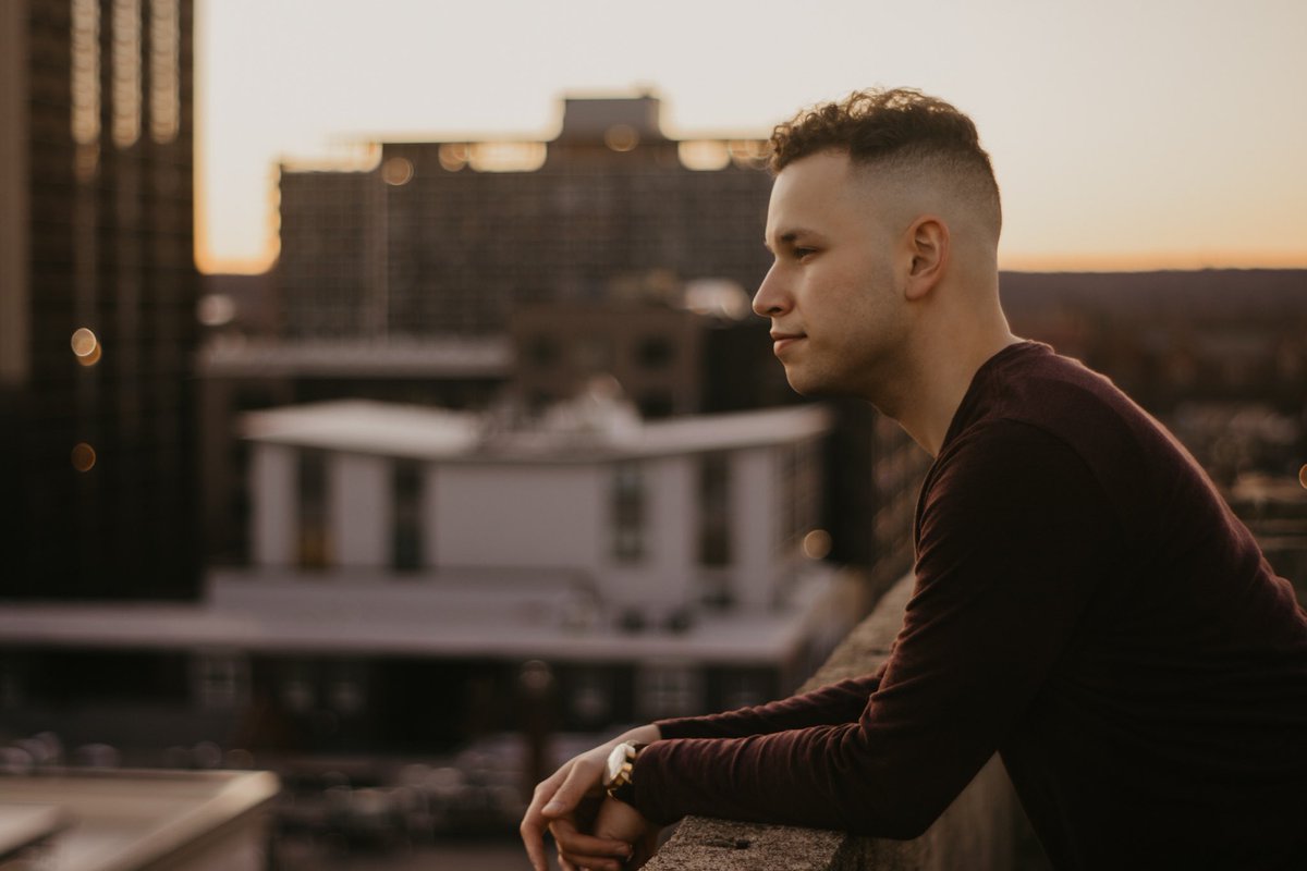 Charlie Widmer is a young man, in this photo standing on a balcony in front of a city skyline.