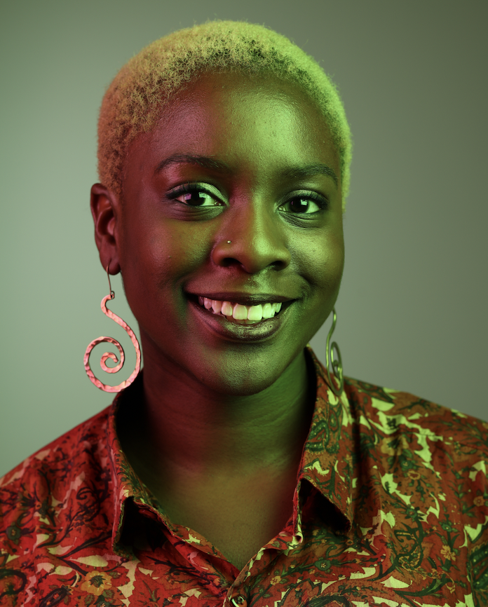 African american woman with blonde hair wearing a red and orange silk shirt and long gold earrings.