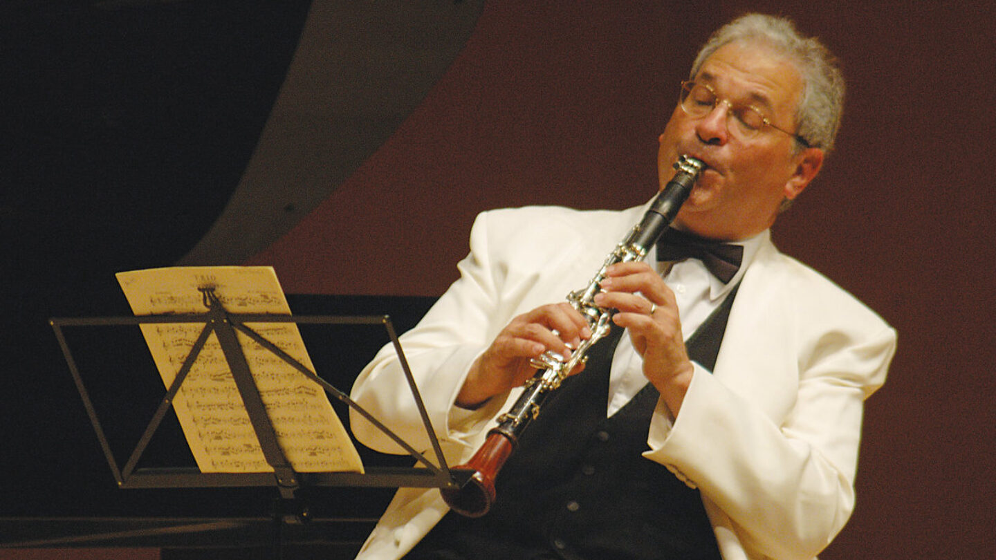 Mr. Shifrin, wearing a white dinner jacket, leans back playing his clarinet up in front of him.