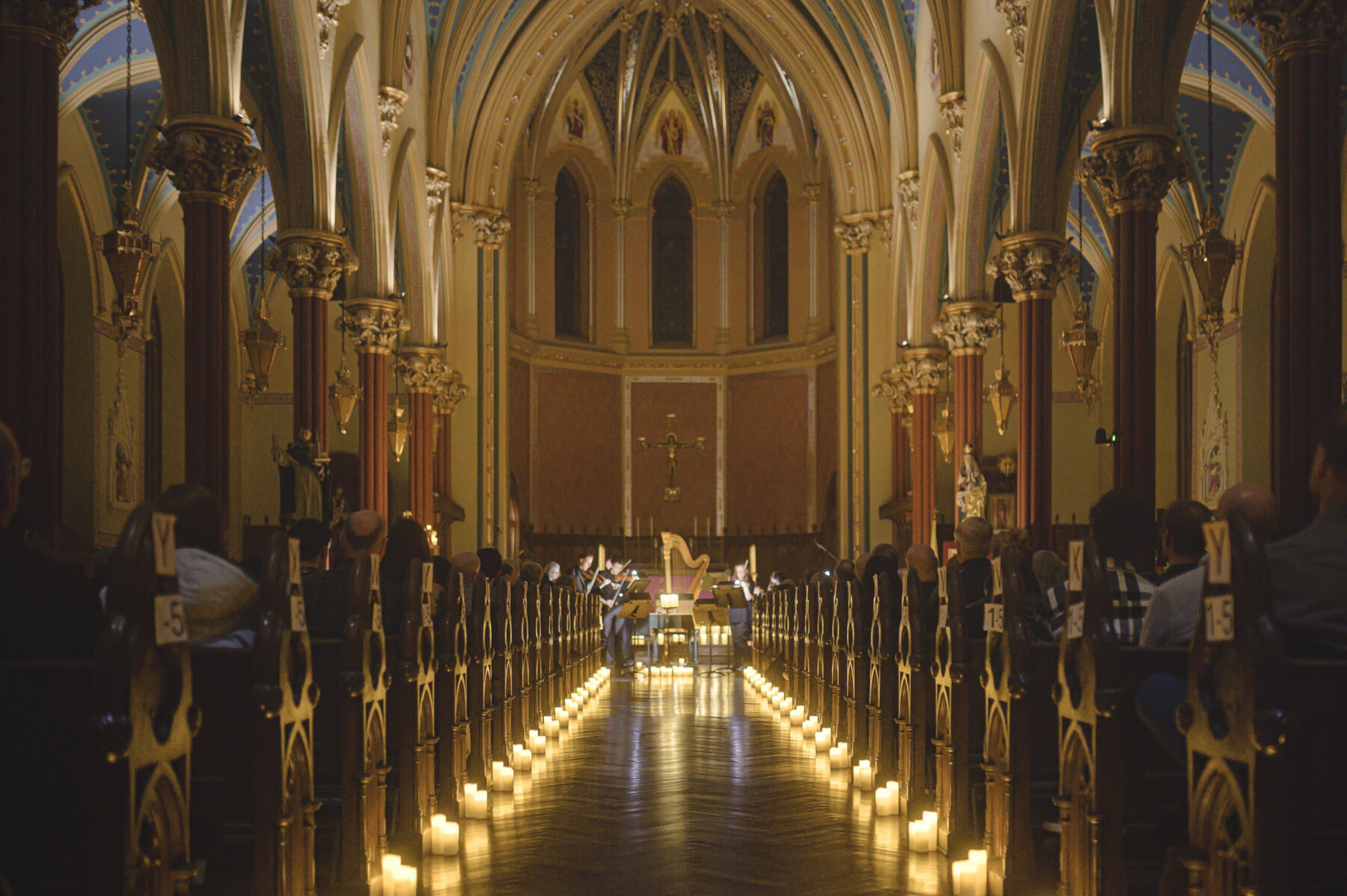 The aisle of St. Mary's church is lined with candles leading to the front of the church, where string musicians play surrounded by candlelight.