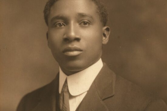 A sepia photograph of composer Robert Nathaniel Dett. He is a Black man wearing a suit with a white, collared shirt and a long neck-tie.