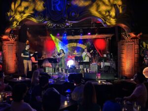 The band DiscoCactus plays on a stage lit up with red, blue, and green lights in a nightclub environment.