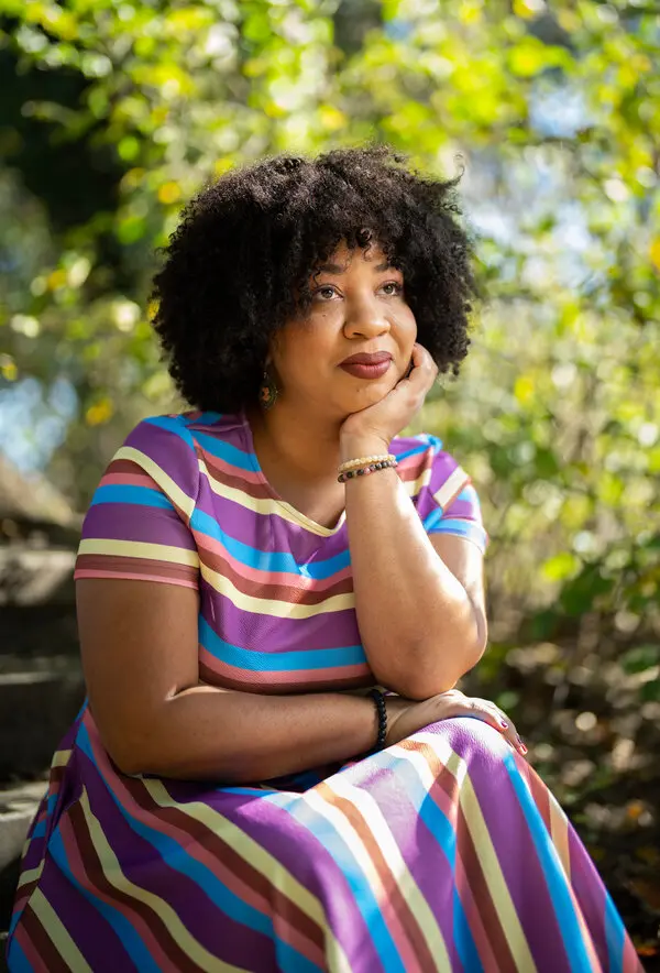 woman with short brown hair sits in nature with her head balanced in her hand.