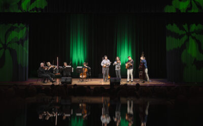 A wide stage with dramatic green lighting. On the left is a string quartet and on the right is a bluegrass band. The energy created by the combination of genres is electric!
